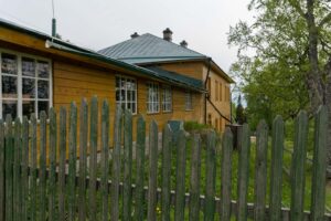 Деревянные корпуса скита на Секирной горе прячутся за старым зеленым забором среди деревьев