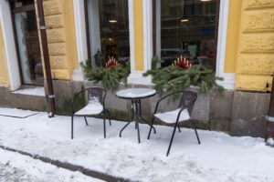 Заснеженный столик и плетёные стулья у украшенных окон кафе